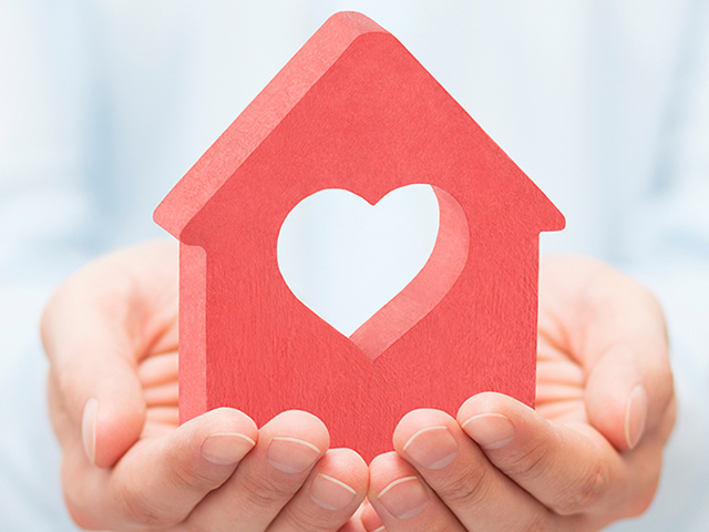 Hands holding a house with a heart cut out of it